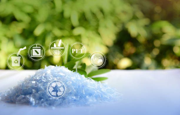 A Pile of PET bottle flakes with green tree blur background. Recycle icon, picking up Plastic Bottle, PET icon&Compress bale icon. Save environment concept. Turning Plastic Bottles into Polyester